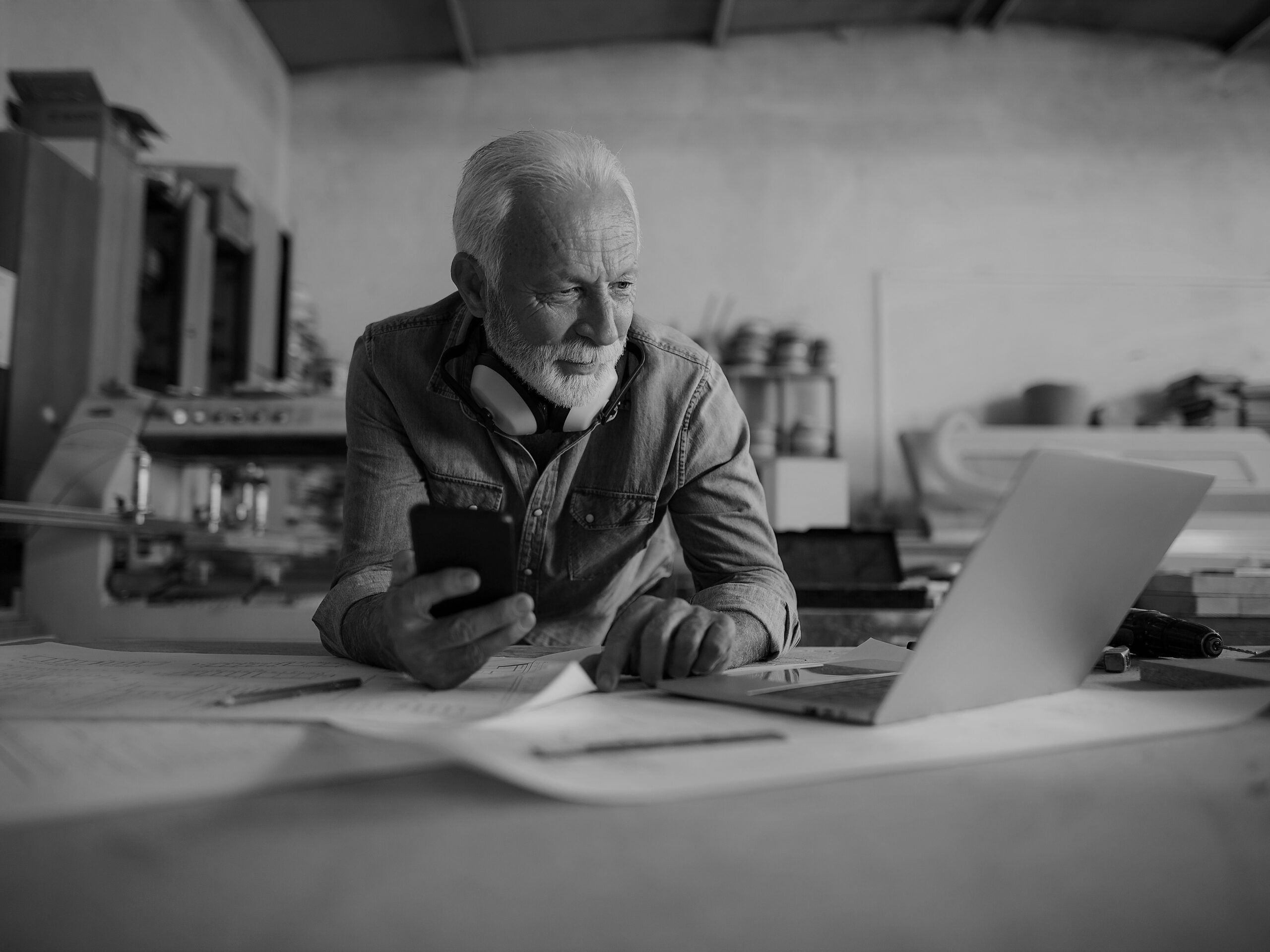 Elderly engineer holding cellphone and looking at the laptop